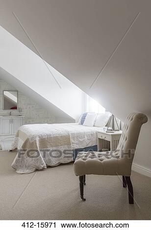 Stock Image - Bed under window in attic bedroom. Fotosearch