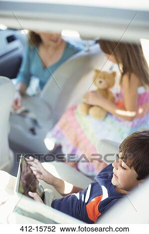 Stock Image - Boy using digital tablet in back seat of car. Fotosearch