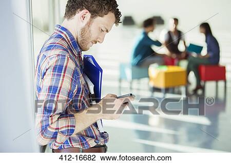 Stock Image - Businessman checking cell phone outside meeting. Fotosearch