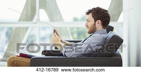 Stock Photo - Businessman using cell phone in lobby. Fotosearch