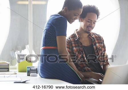 Stock Image - Casual businessman and businesswoman using laptop in meeting. Fotosearch