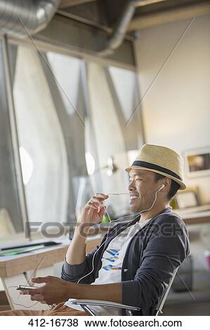 Casual businessman using hands-free device with cell phone in office View Large Photo Image Stock Photo - Casual businessman using hands-free device with cell phone in office. Fotosearch