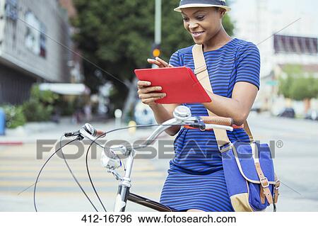 Casual businesswoman using digital tablet on bicycle on urban street View Large Photo Image Stock Photograph - Casual businesswoman using digital tablet on bicycle on urban street. Fotosearch