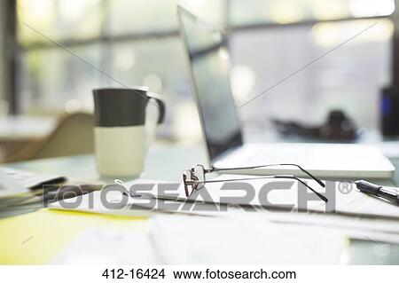 Close up of coffee cup and eyeglasses on paperwork near laptop View Large Photo Image Picture - Close up of coffee cup and eyeglasses on paperwork near laptop. Fotosearch