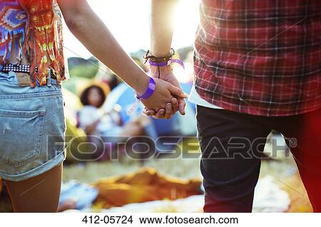 Picture - Close up of couple holding hands outside tents at music festival. Fotosearch