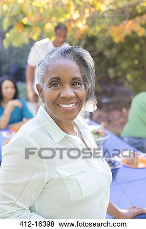 Stock Photo - Close up portrait of smiling senior woman on patio with family in background. Fotosearch