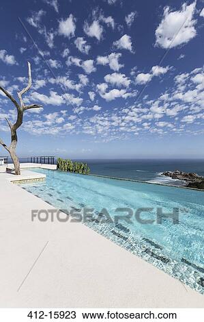 Stock Image - Clouds in blue sky over luxury lap pool overlooking ocean. Fotosearch