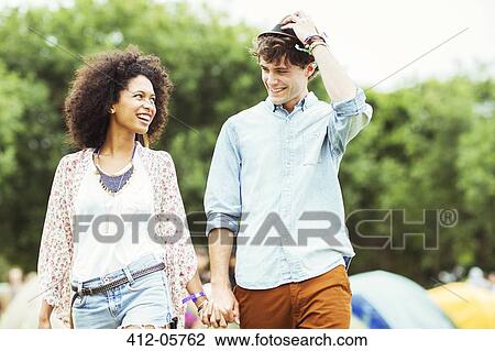 Stock Image - Couple holding hands outside tents at music festival. Fotosearch