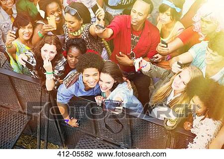 Stock Image - Couple taking self-portrait with camera phone at music festival. Fotosearch