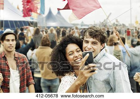 Stock Photo - Couple taking self-portrait with camera phone at music festival. Fotosearch