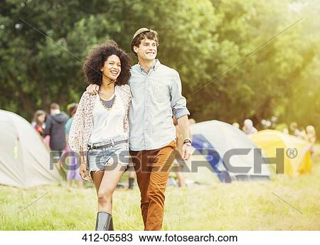Stock Image - Couple walking outside tents at music festival. Fotosearch