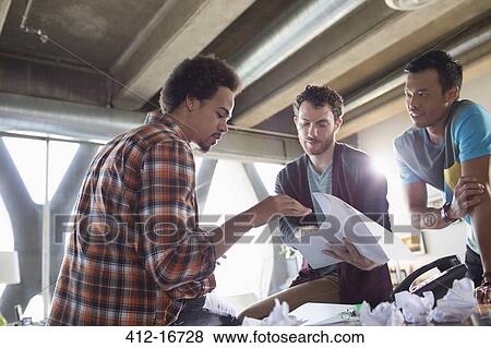 Stock Photo - Creative businessmen discussing paperwork in meeting. Fotosearch