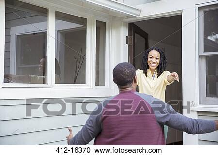Stock Image - Enthusiastic woman greeting man in doorway. Fotosearch