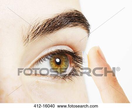Stock Image - Extreme close up of woman putting contact lens into eye. Fotosearch