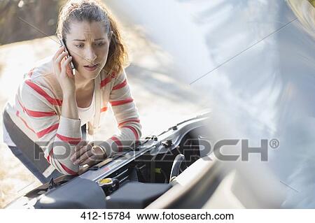 Frustrated woman talking on cell phone and looking at car engine at roadside View Large Photo Image Picture - Frustrated woman talking on cell phone and looking at car engine at roadside. Fotosearch