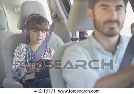 Girl with headphones using digital tablet inside car View Large Photo Image Stock Image - Girl with headphones using digital tablet inside car. Fotosearch