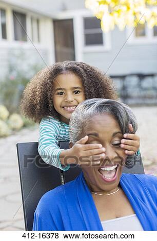 Stock Photo - Granddaughter surprising grandmother on patio. Fotosearch