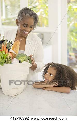 Grandmother and granddaughter unpacking groceries in kitchen View Large Photo Image Stock Image - Grandmother and granddaughter unpacking groceries in kitchen. Fotosearch