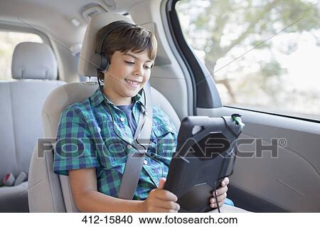 Stock Image - Happy boy using digital tablet in back seat of car. Fotosearch