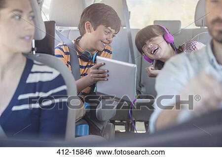 Stock Photograph - Happy brother and sister using digital tablet in back seat of car. Fotosearch