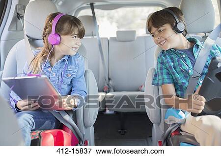 Stock Photo - Happy brother and sister with headphones using digital tablets in back seat of car. Fotosearch