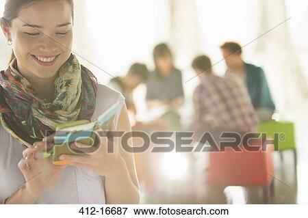Stock Photo - Happy businesswoman text messaging with cell phone outside meeting. Fotosearch