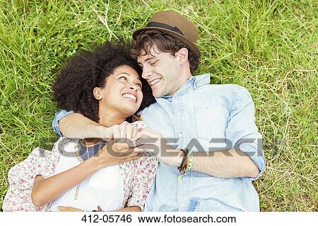 Happy couple holding hands and laying in grass View Large Photo Image Stock Photograph - Happy couple holding hands and laying in grass. Fotosearch