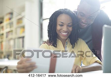 Stock Photo - Happy couple reading paperwork at laptop. Fotosearch