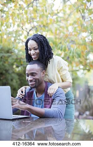 Happy couple using laptop at patio table View Large Photo Image Picture - Happy couple using laptop at patio table. Fotosearch