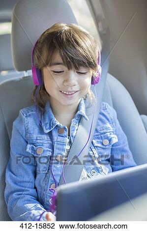 Happy girl with headphones using digital tablet in car View Large Photo Image Stock Image - Happy girl with headphones using digital tablet in car. Fotosearch