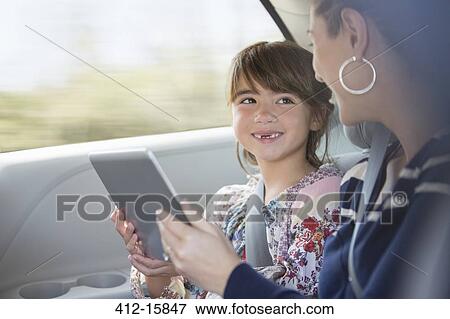 Happy mother and daughter using digital tablet in back seat of car View Large Photo Image Stock Photo - Happy mother and daughter using digital tablet in back seat of car. Fotosearch