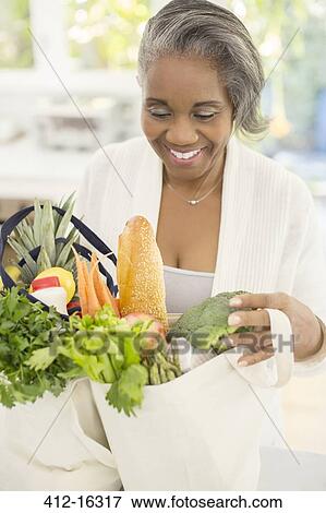 Stock Photo - Happy senior woman unpacking groceries. Fotosearch