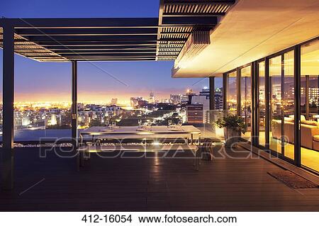 Picture - Illuminated luxury house and patio overlooking city. Fotosearch