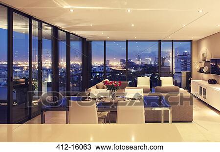 Stock Image - Illuminated modern living room overlooking city. Fotosearch