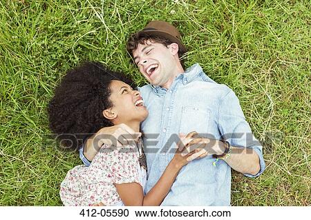 Stock Image - Laughing couple laying in grass. Fotosearch