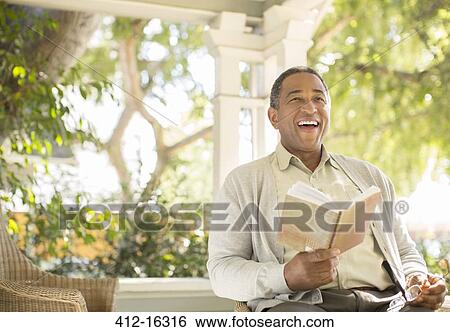 Laughing senior man reading book on porch View Large Photo Image Stock Photograph - Laughing senior man reading book on porch. Fotosearch