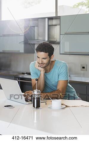 Man drinking coffee and using laptop in kitchen View Large Photo Image Stock Image - Man drinking coffee and using laptop in kitchen. Fotosearch