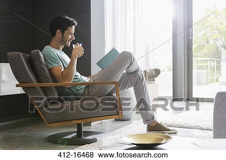 Man drinking tea and reading book in living room View Large Photo Image Stock Photo - Man drinking tea and reading book in living room. Fotosearch