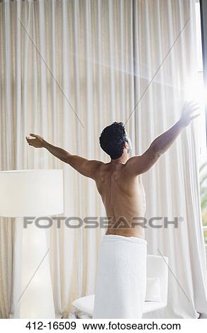 Stock Photo - Man in towel basking in sunlight at window. Fotosearch