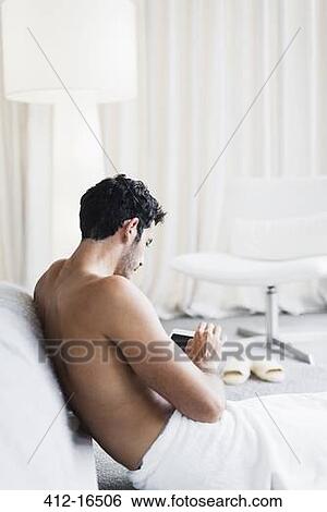 Stock Photograph - Man in towel using digital tablet in bedroom. Fotosearch