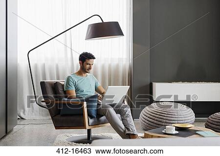 Man using laptop in living room View Large Photo Image Stock Image - Man using laptop in living room. Fotosearch