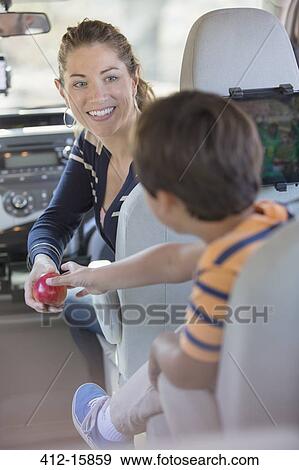 Mother giving boy an apple inside car View Large Photo Image Stock Photo - Mother giving boy an apple inside car. Fotosearch