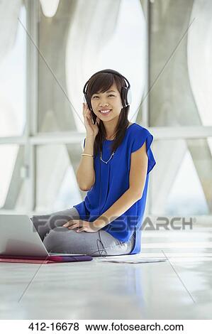 Stock Photo - Portrait of casual businesswoman using laptop and wearing headphones on floor. Fotosearch