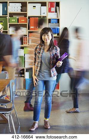 Picture - Portrait of confident casual businesswoman with co-workers rushing by in background. Fotosearch