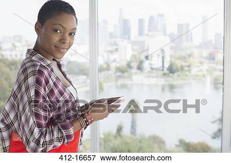 Portrait of confident casual businesswoman holding cell phone at urban window View Large Photo Image Stock Photo - Portrait of confident casual businesswoman holding cell phone at urban window. Fotosearch