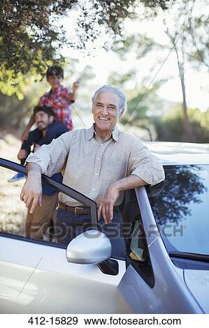 Stock Photo - Portrait of confident senior man leaning against car. Fotosearch