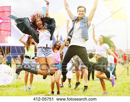 Stock Image - Portrait of enthusiastic friends jumping and dancing at music festival. Fotosearch