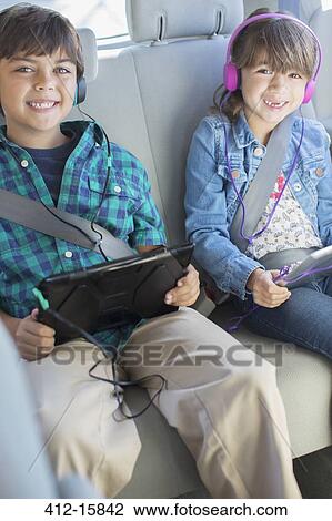 Portrait of happy brother and sister with headphones using digital tablets in back seat of car View Large Photo Image Stock Image - Portrait of happy brother and sister with headphones using digital tablets in back seat of car. Fotosearch