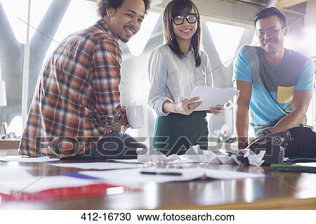 Stock Image - Portrait of happy creative business people with paperwork in meeting. Fotosearch