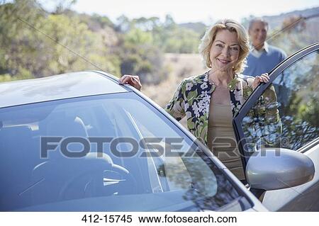 Stock Photography - Portrait of happy senior woman leaning on car. Fotosearch